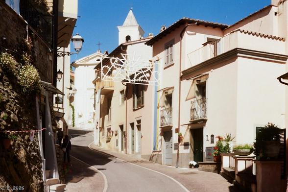 Farbfoto der Hauptstraße der Kleinstadt Gerano in Lazio, Italien. Zwischen den historischen Häusern ist eine weiße Dekoration aufgehängt, die in etwa die Form eines stilisierten Weihnachtsbaums hat. Ist aber für die alljährliche Gartenschau gedacht. Olympus 35 SP auf Kodak ProImage 100-Film.