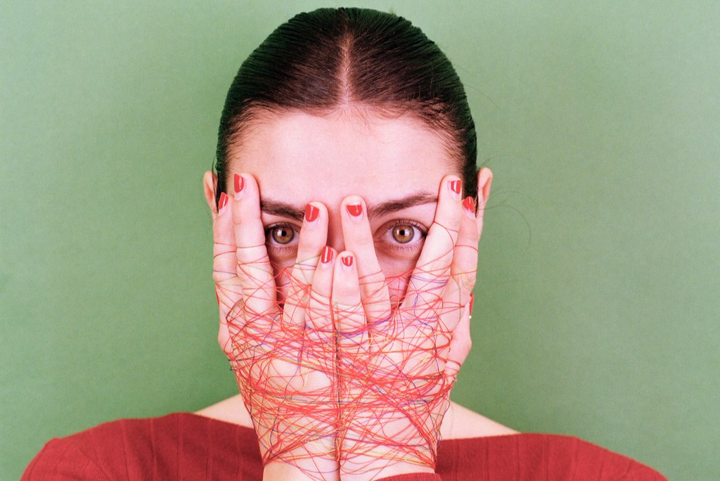 Una joven se tapa el rostro con las manos atadas con hilos de color rojo.