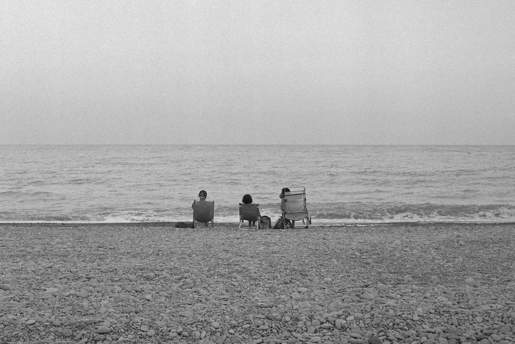 Tres personas sentadas mirando el
mar en la orilla de una playa. Blanco y negro.