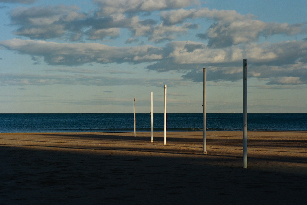 Una platja amb posts blancs on es projecta llum i ombra i núvols.